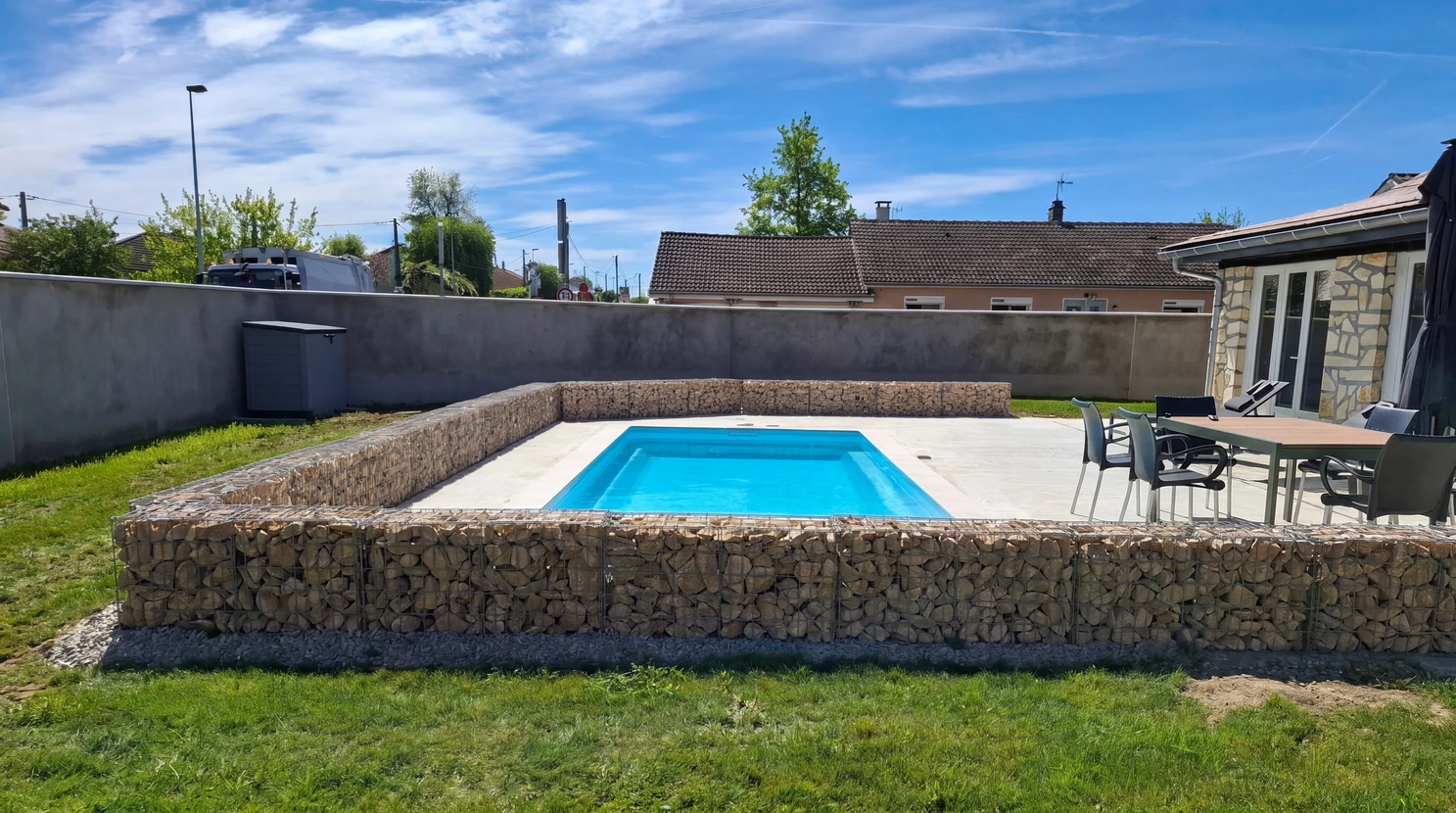 Piscine rectangulaire à coque polyester bleue, semi-enterrée, surélevée sur une plateforme en béton ciré